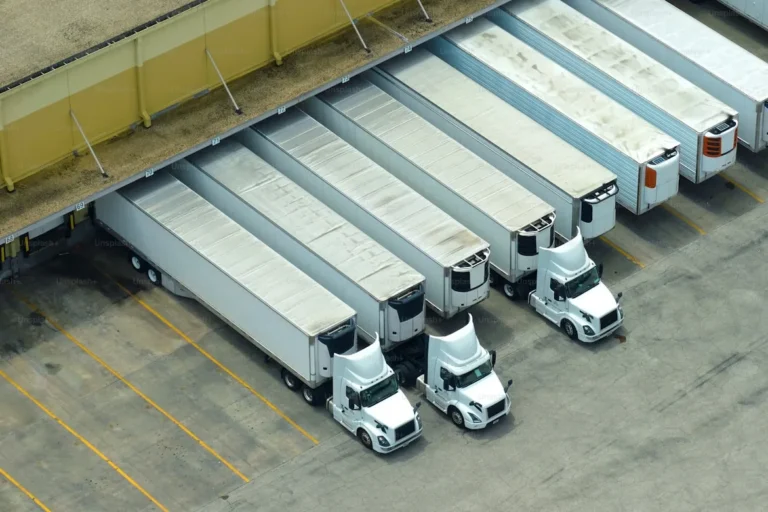 Aerial view of multiple semi-trucks docked at a warehouse loading bay, representing the logistics and shipping stage of industrial packaging and freight distribution