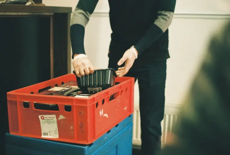 Hand sorting items into red and blue stacked storage crates